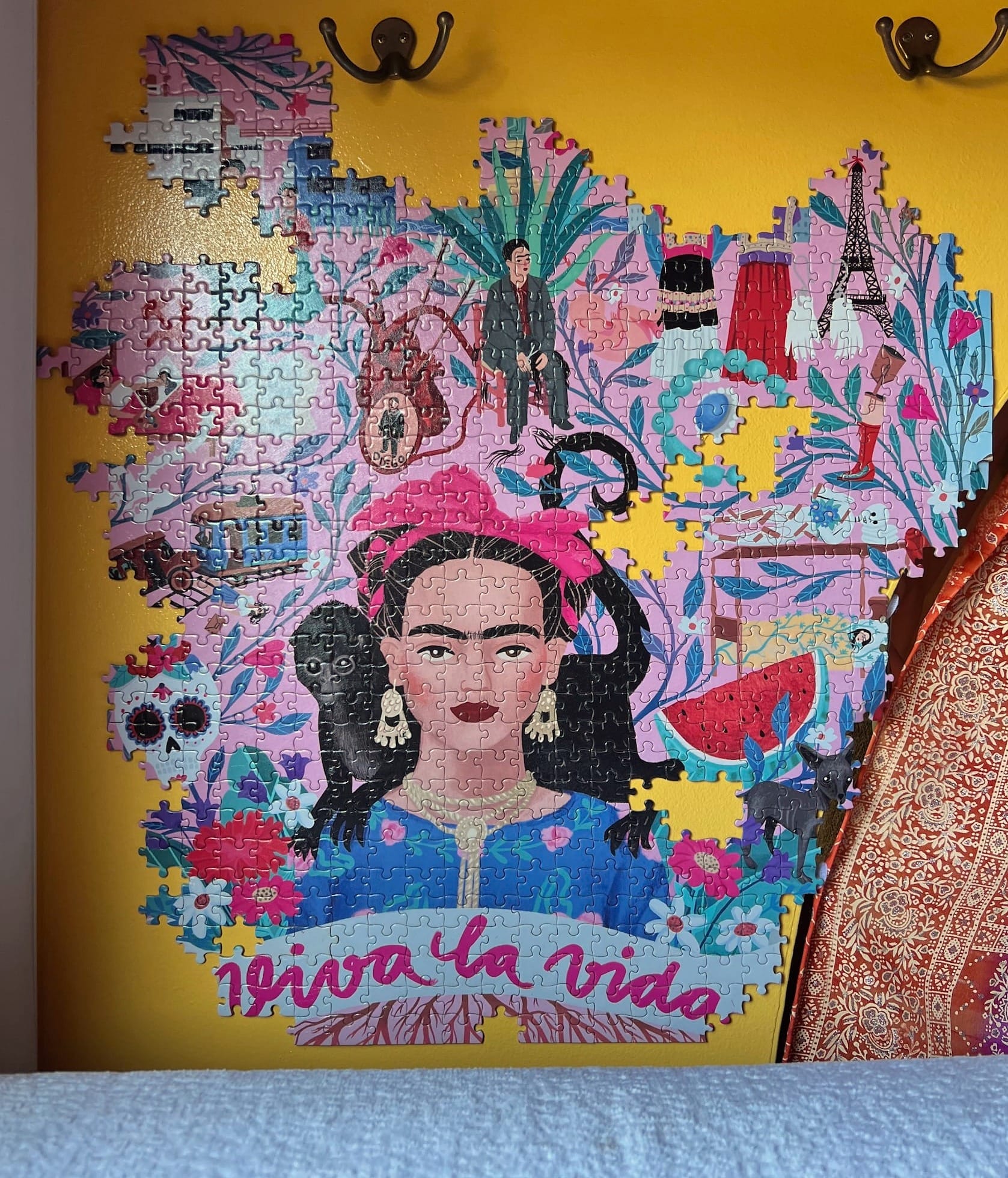 A puzzle featuring Frida Kahlo hanging on a yellow wall, with many pieces missing from the edges and center.