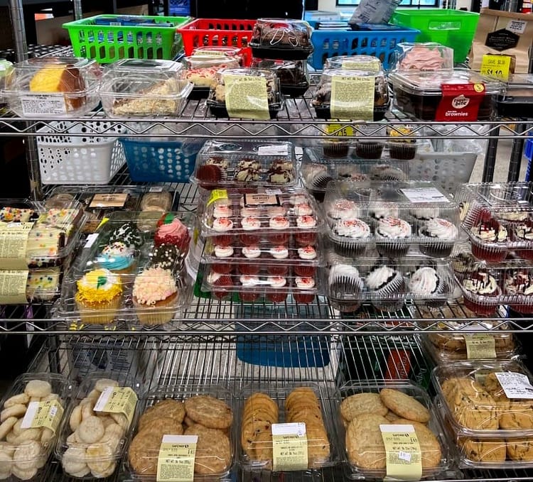 A grocery-store rack packed with containers of cookies, cupcakes, and slices of cake